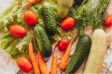 Fresh vegetables on a table: cucumbers, tomatoes, carrots, greens	