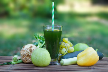 Healthy green smoothie with apples, grapes, cucumber and celery. Fruit and vegetable juice on wooden table, with blured nature in  background. Homemade green smoothie in glass with a straw.