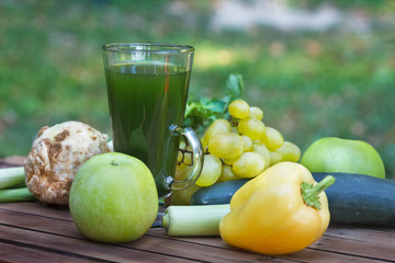 Healthy green smoothie with apples, grapes, cucumber and celery. Fruit and vegetable juice on wooden table, with blured nature in  background. Outdoor image.