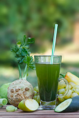 Healthy green smoothie with fruits and vegetables juice on wooden table, with blured nature in  background. Homemade green smoothie in glass with a straw. Vertical image.