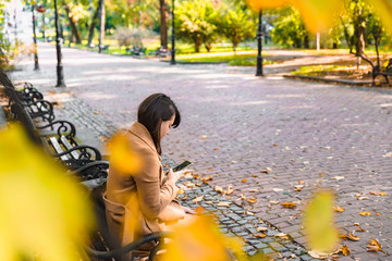 young adult fashion woman sitting at city park bench in autumn fall season