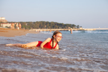 young beautiful girl in glasses and a red bathing suit lies on the beach and plays in the waves