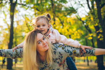 piggyback mother playing with daughter at autumn city park