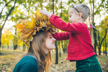 young mother make maple leaf wreath for little toddler daughter