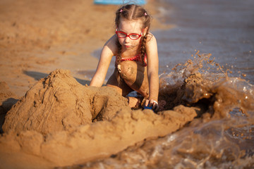 young girl in a red bathing suit and glasses plays on the beach. sand castle