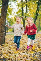 two little girls girlfriends playing at autumn city park holding hands