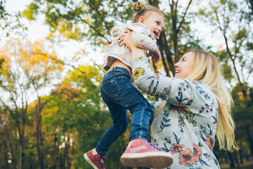 mather with little toddle daughter playing in autumn city public park