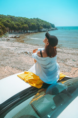 happy woman at sea summer beach sitting at car hood