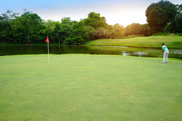 Fototapeta na wymiar Golfer playing golf into the hole in beautiful golf course. The evening golf course with sunset in thailand