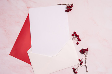 Autumn romantic composition. Paper blank, envelope, branches with red hawthorn berries on a pink background.