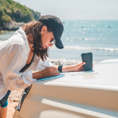 woman checking map on car hood drinking coffee at summer sea beach
