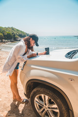 woman checking map on car hood drinking coffee at summer sea beach
