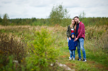 Naklejka na ściany i meble Mom, dad and little son are standing on a country road in the summer afternoon. Parents smile warmly and look at their son
