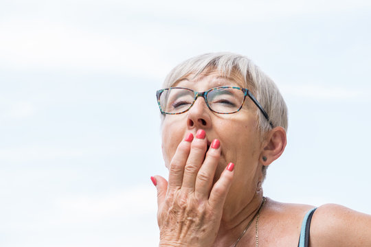 65 Years, Older Woman With White Hair And Glasses With Hand In His Mouth, Yawning