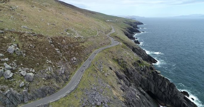 Pan left aerial, people drive motorcycles on Dingle Peninsula