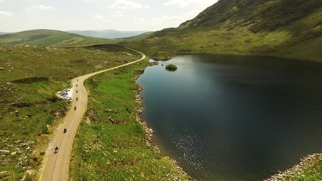Motorcycles drive past lake in Irish countryside, aerial
