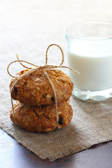 Two oatmeal cookies tied with rope and glass with milk on burlap tablecloth.