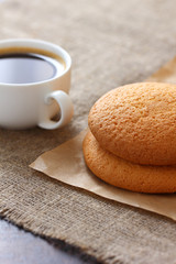 Oatmeal cookies on kraft paper, white mug with coffee on burlap, tablecloth