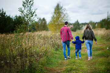 Fototapeta premium Parents walk with their little son on a country road, rear view. Copy space