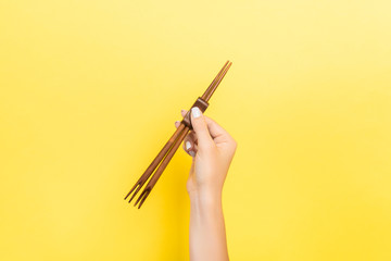 Female hand holding chopsticks on yellow background. Sushi concept with empty space for your idea