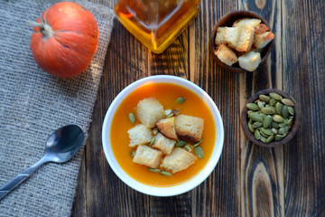 Pumpkin soup with croutons and seeds in a bowl on a wooden table