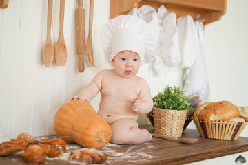 little baker baby child in chef hat at kitchen table alone with orange big pumpkin 