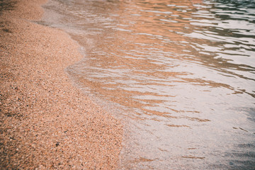 Sea beach in the tropics and the soft wave of the blue ocean. Summer gloomy day and sandy beach with stones background. The concept of summer vacation.