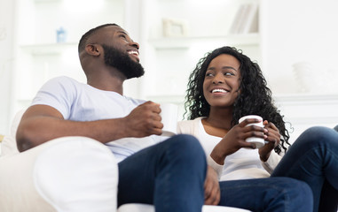 Obraz premium Cheerful black couple relaxing with cup of coffee at home