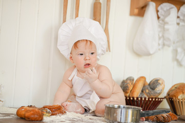 little baker child in chef hat at kitchen table alone