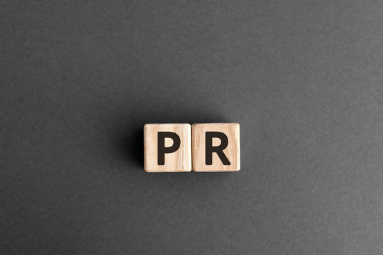 PR - wooden blocks with letters, public relations PR concept,  top view on grey background
