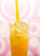 Pouring Orange juice into glass against a pink funky background