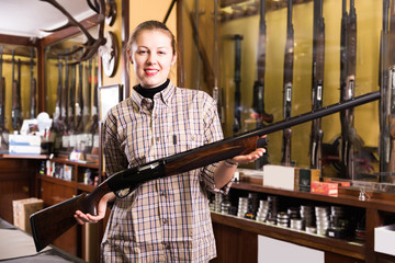 Fototapeta na wymiar Young smiling saleswoman in gun shop showing rifle