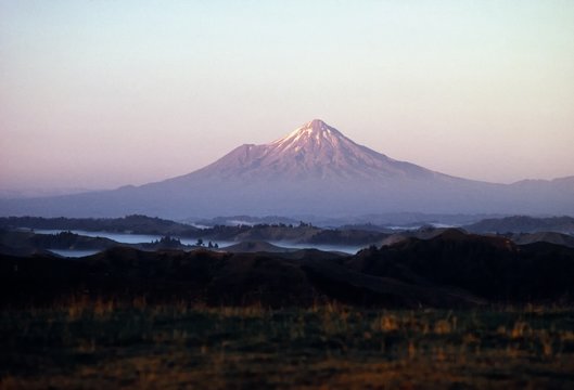 A large mountain with a peak and dark in the front.