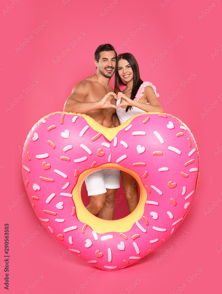 Poster Young attractive couple in beachwear with inflatable ring on pink background