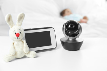 Baby monitor, camera and toy on table near bed with child in room. Video nanny