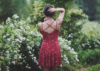 A person wearing a red dress standing in front of a white flowery bush