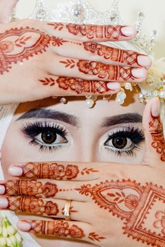 A woman with henna tattoos on her hands covers her mouth.