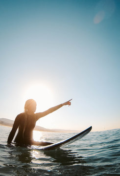 A young woman straddles a surfboard in the ocean.