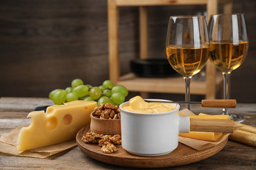 Pot of tasty cheese fondue and products on wooden table