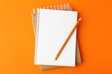 Notebooks with pencil on orange background, top view