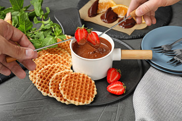 People dipping strawberries into fondue pot with milk chocolate at table, closeup