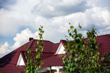 View through tree of red roof, on background of blue sky with clouds.