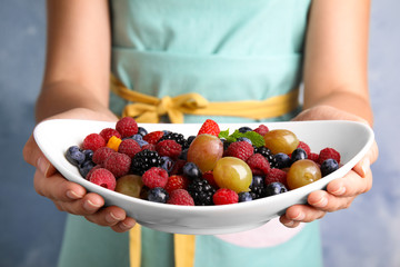 Woman holding plate of fresh tasty fruit salad against blue background, closeup