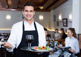 Portrait of smiling waiter with serving tray meeting restaurant guests