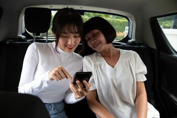 Cheerful Asian mother and daughter sitting in car and touching mobile phone, Going on a trip and different generations senior elderly and teenager concept