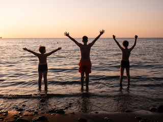 Fototapeta premium Free happy boys raising arms watching the sun in the background at sea sunrise, teenager on sea