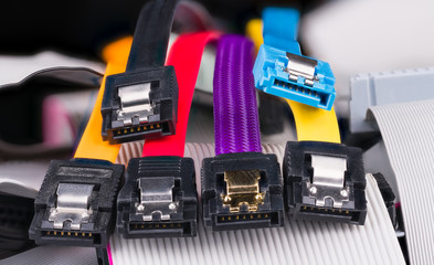 Internal serial connectors with colorful flat cables on pile of obsolete parallel cords. Computer bus interface for storage devices as hard, optical or solid-state disk drives. Data transfer hardware.