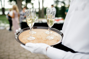 Handsome young butler holding silver tray with two glasses of champagne