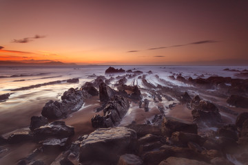 Obraz premium Rock formation at barrika beach in spain. Water flowing around rocks at sunset. Very dramatic and moody red sunset light.