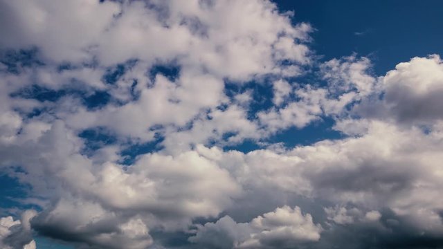 Timelapse. White and gray clouds slowly float across the blue sky during the day.